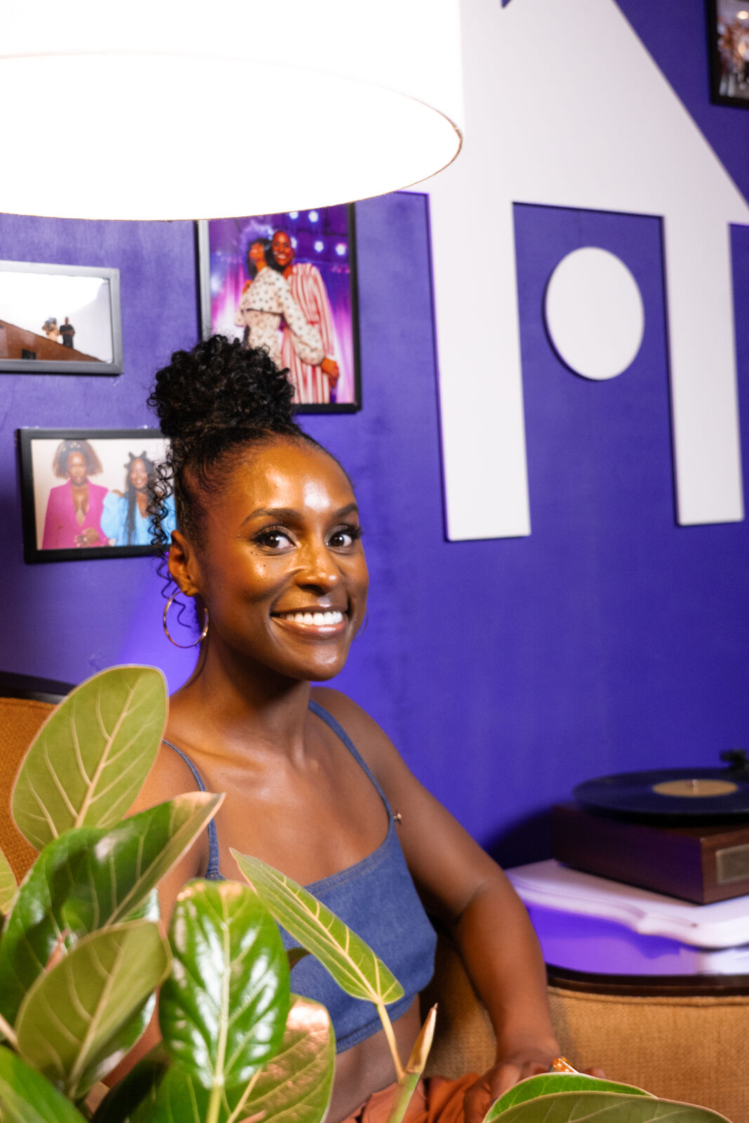 Issa Rae seated against the purple HOORAE wall, framed by a fiddle leaf plant