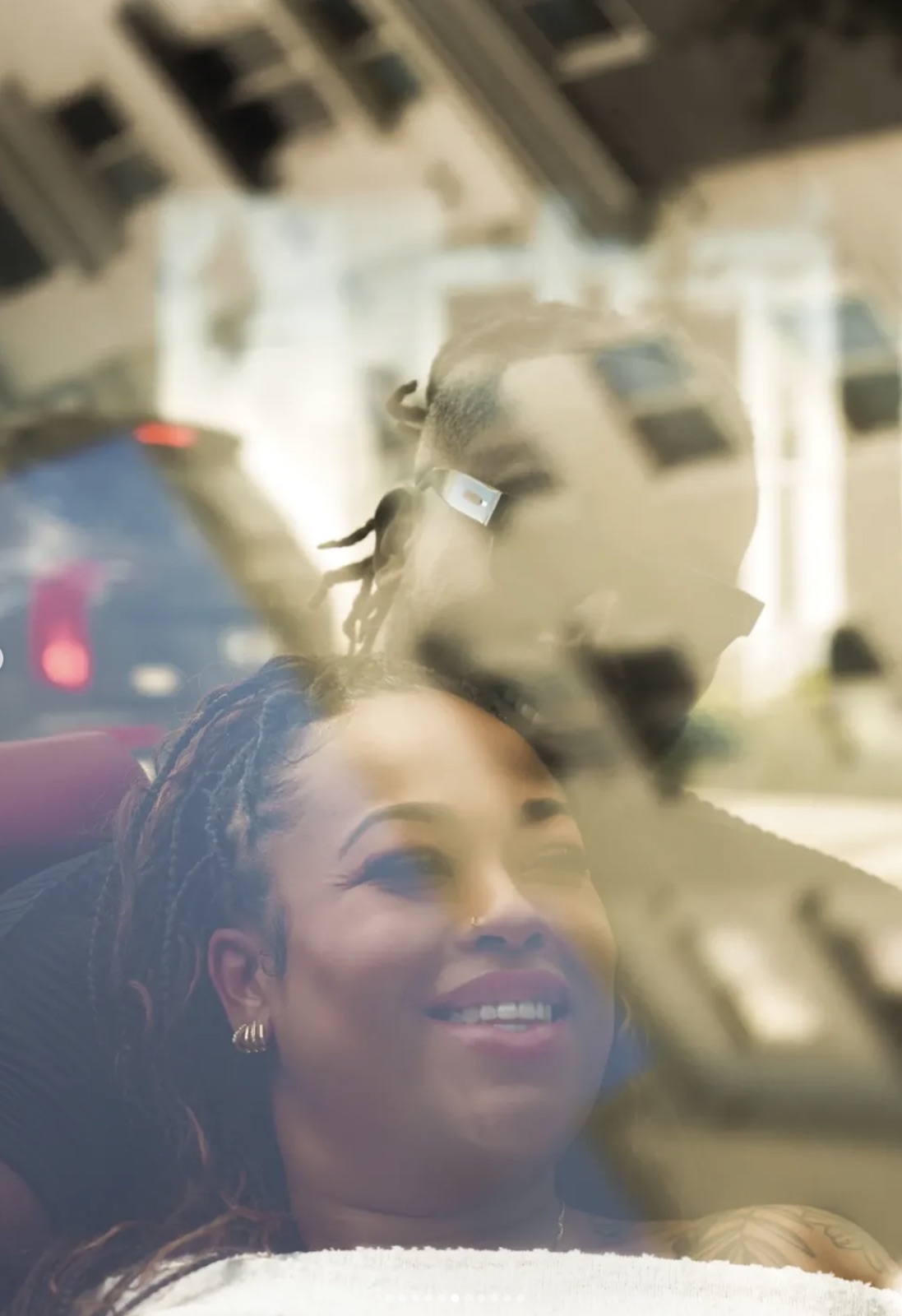 A woman laughing through the reflection of the city in a car window