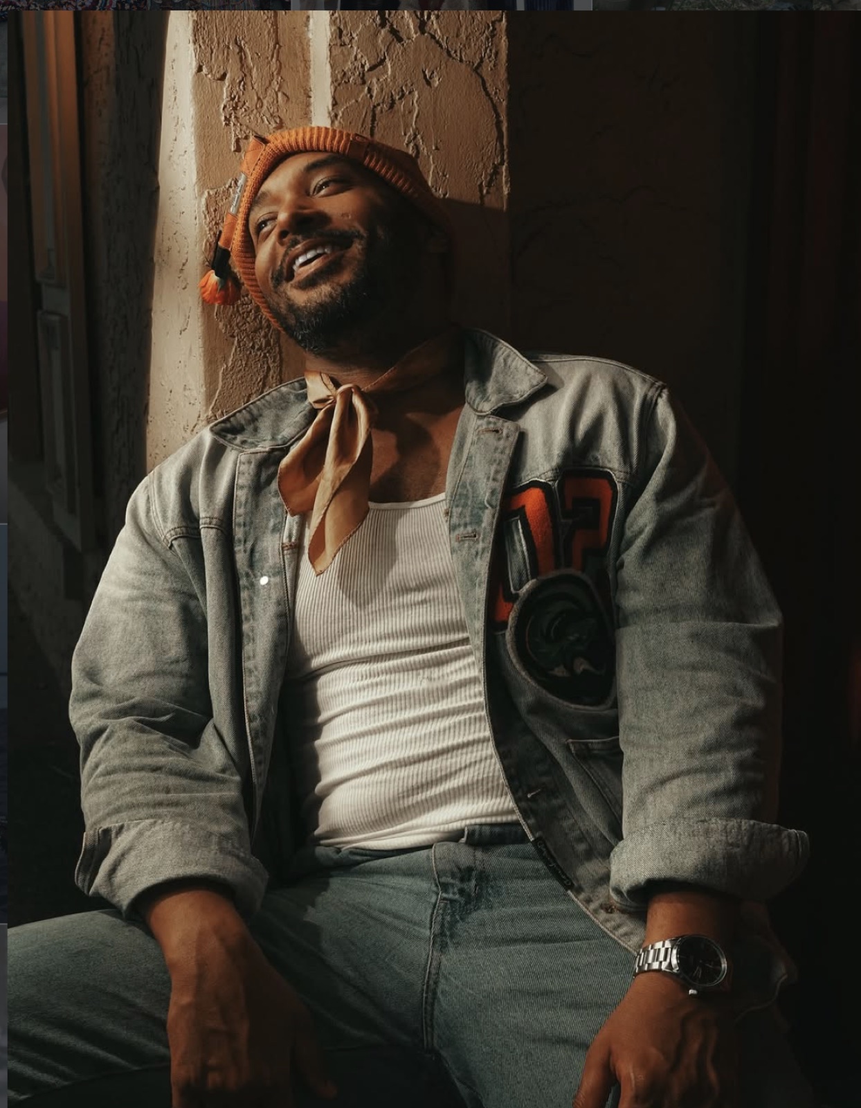 Man laughing in denim and an orange beanie in warm window light