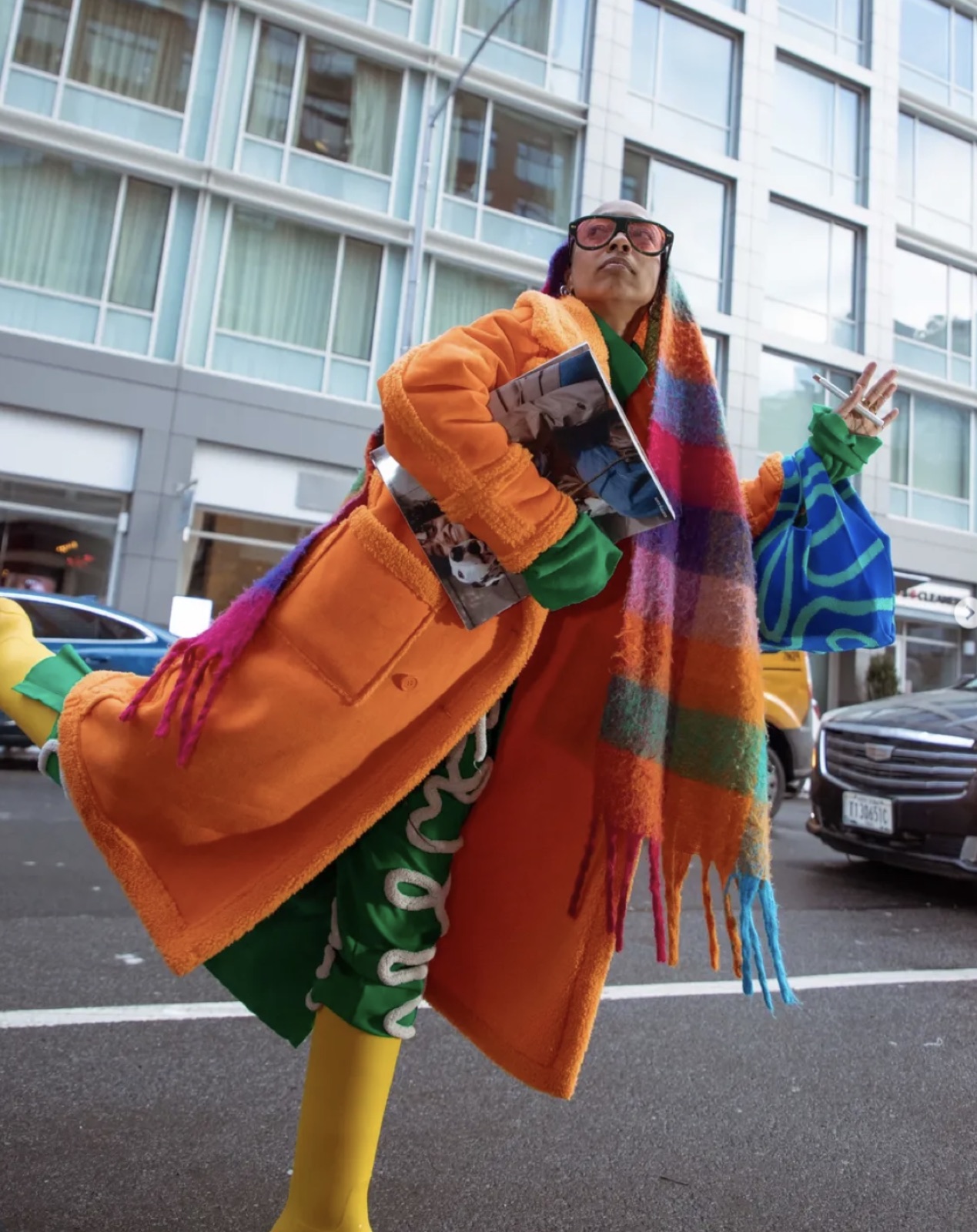 Jade mid-stride on the street in a rainbow plaid coat and yellow tights