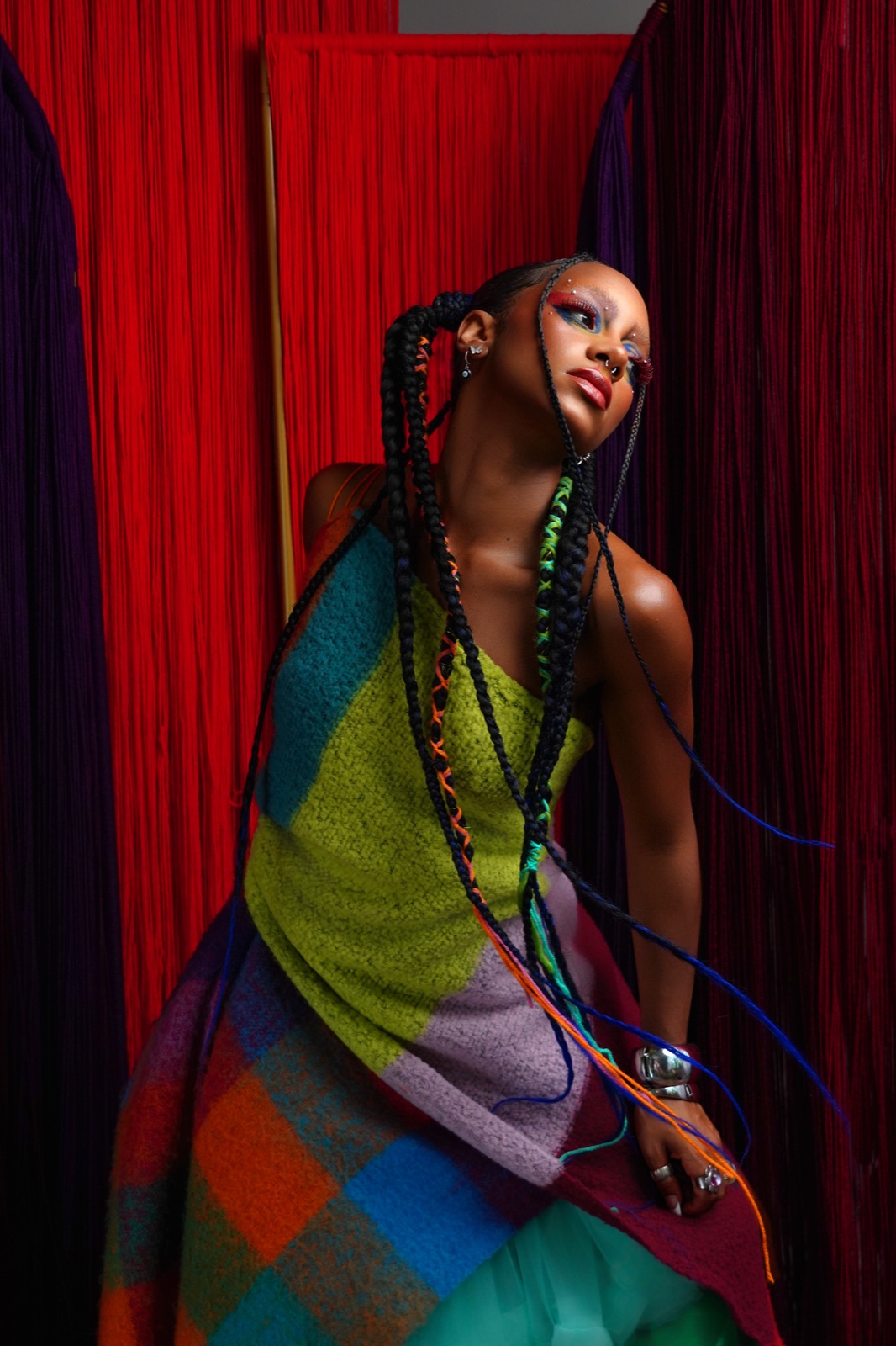 Portrait in a striped knit dress and beaded braids against a red curtain