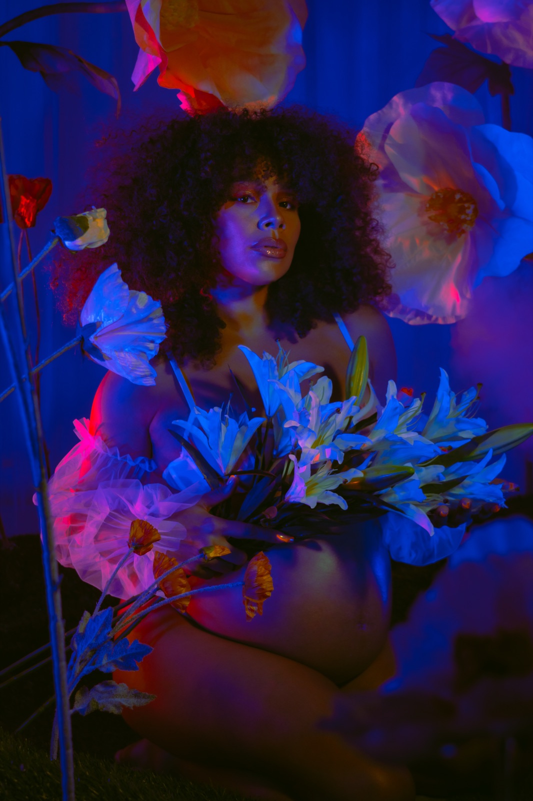 Portrait among blue-lit paper florals, petals at the shoulders