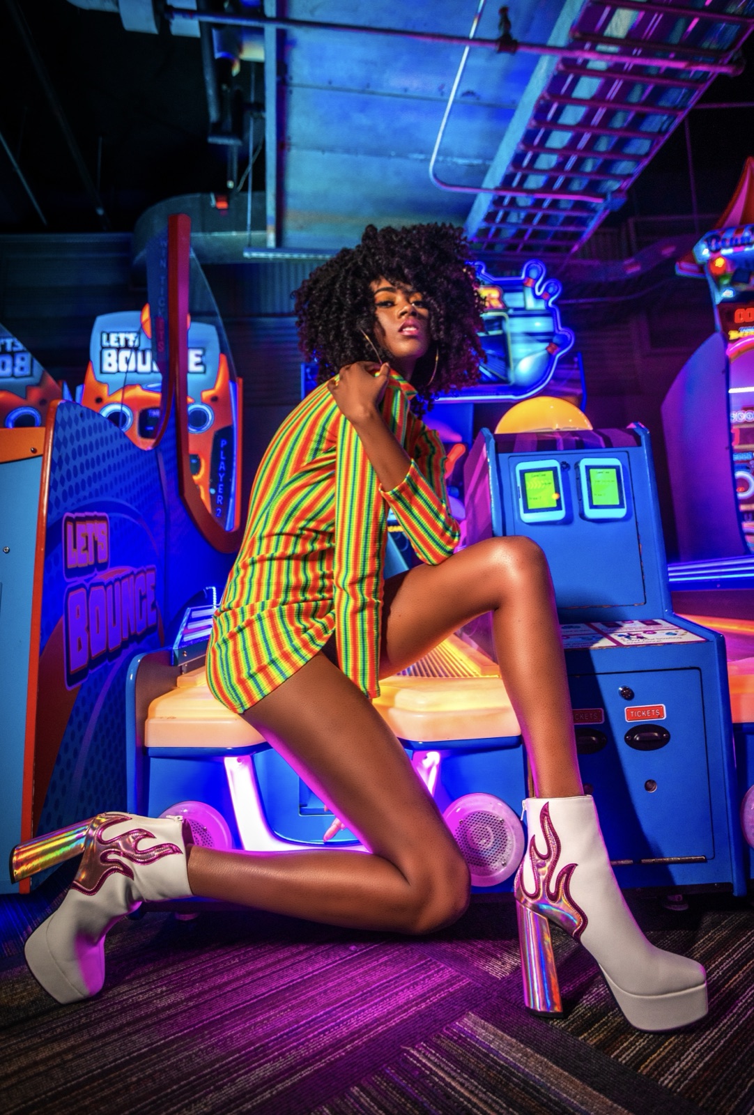 Portrait in a green striped dress astride a neon arcade machine