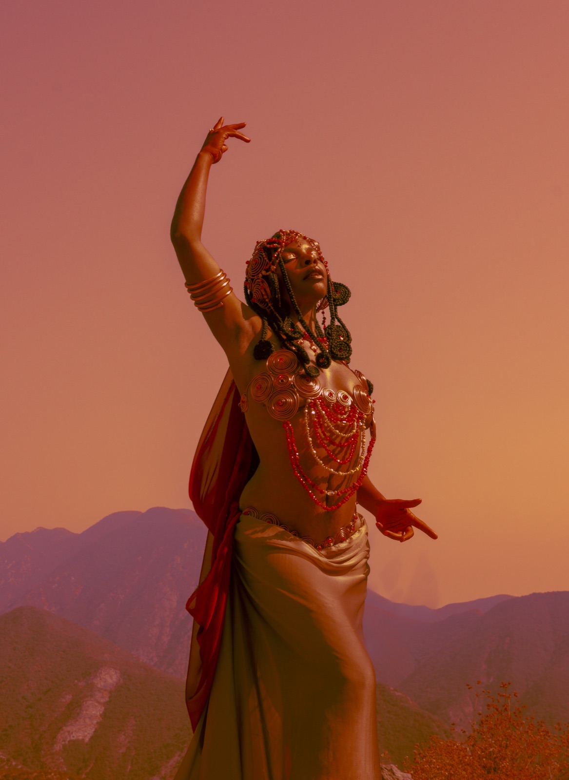 A dancer in gold reaching skyward against a burnt sunset