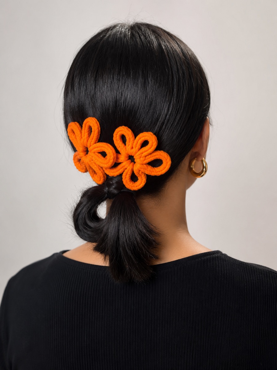 Two orange knit flowers worn in dark swept-back hair