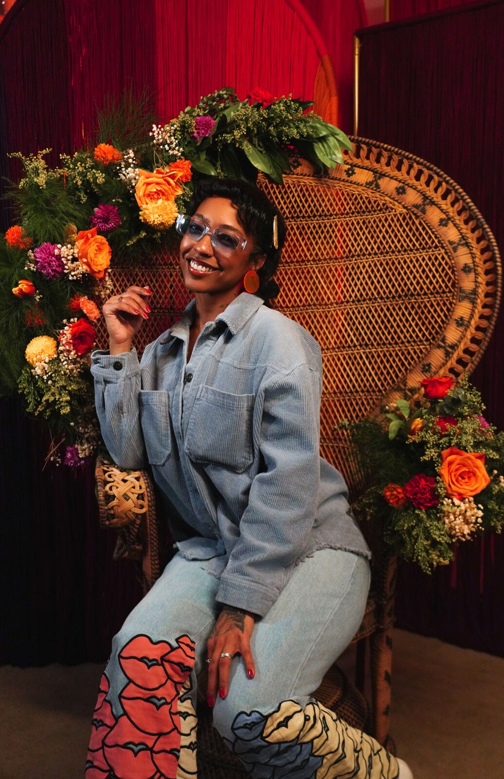 A guest in denim on the garlanded peacock chair against poured red yarn