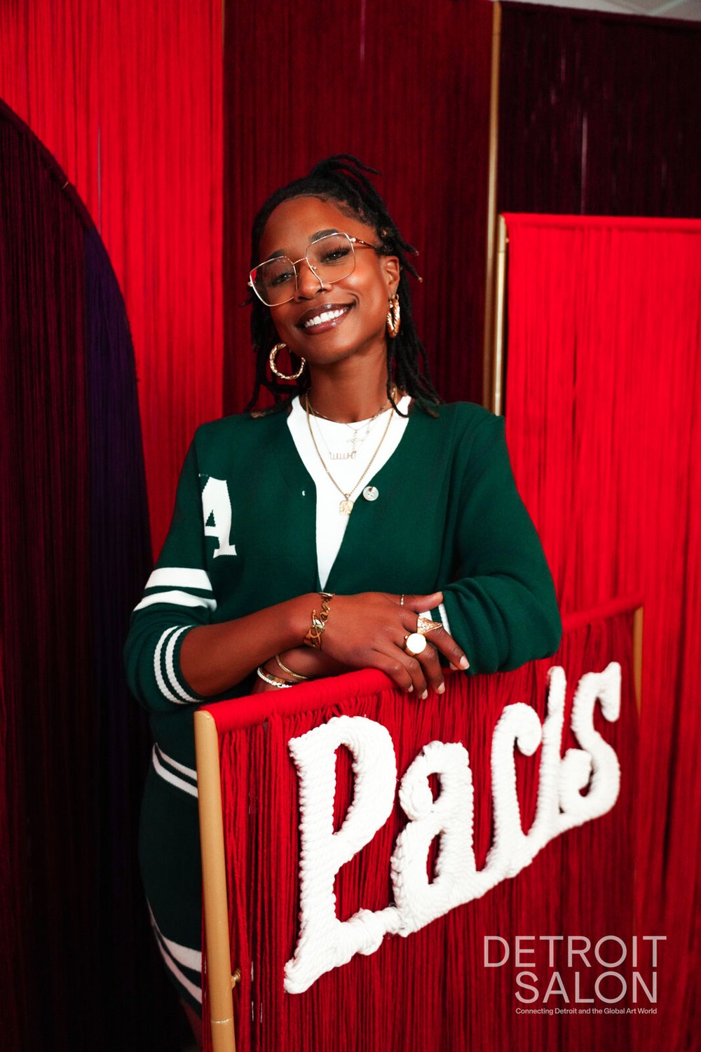 A guest in a green varsity cardigan leaning on the yarn Paris marquee between red fringe arches