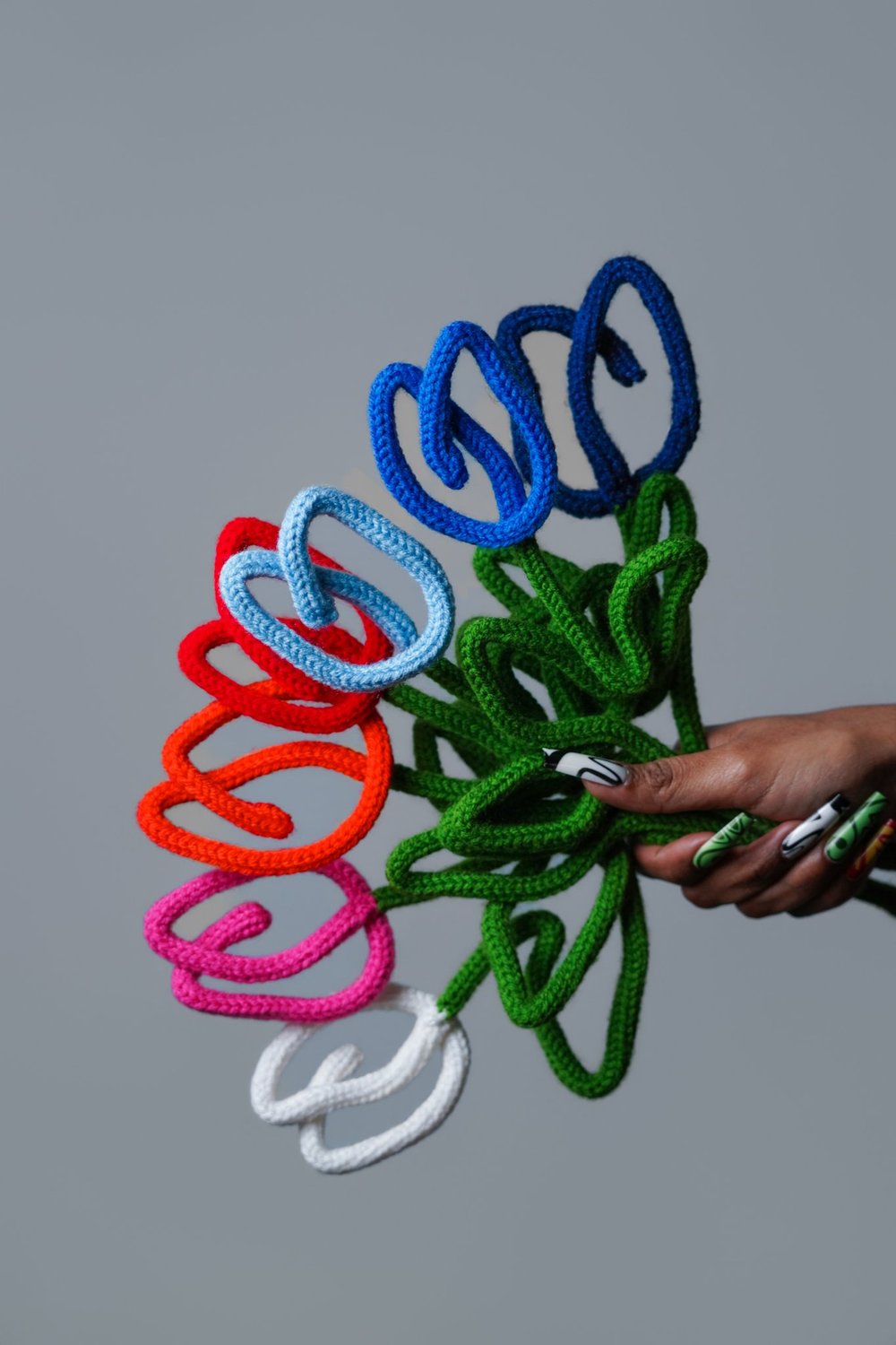 A hand holding a bouquet of rainbow crocheted tulips against gray